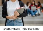 Small photo of Close up young female college students torso holding document files with blurry university campus and other students. Outdoor. Concept for education, college students life.