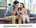 Small photo of Millennial Asian unhappy family mother sitting on sofa couch holding hugging soothing little young female daughter while sad stressed father crying after big fight argument in living room at home.