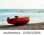 Small red rowboat with sculls lying at shore of the sea