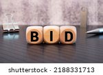 Small photo of three wooden cubes with letters BID, on white table and diagram, business concept