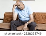 Small photo of Tired, depressed senior man sitting on couch in living room feeling hurt and lonely. Aged, white-haired man touching forehead suffering from severe headache or recalling bad memories