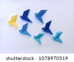 Seven blue origami  birds are flying leading by a yellow bird , isolated on white.