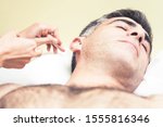 Small photo of Closeup picture of an arm stabbing an acupuncture needle in the man's earlobe who lying on table. Closeup of his head, ear and stab with needle