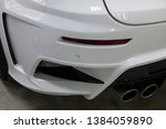 Small photo of The rear bumper of a tuned car is white with a double exhaust nozzle, a diffuser and a red reflector in a vehicle tuning workshop. Auto service industry