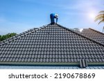 Roof repair, worker replacing gray tiles or shingles on house with blue sky as background and copy space, Roofing - construction worker standing on a roof covering it with tiles.