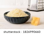 Small photo of Grated parmesan or grana padano in a ceramic bowl and piece of hard cheese on a white wood table. Delicious ingredient for pizza, sandwiches, salads. Traditional dairy product. Front view.