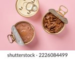 Wet cat food in open jars over pastel pink background. Wet pet feed in metal cans closeup. Canned meat pieces and soft pate for carnivore domestic animals. Сat food concept. Top view.