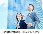 Small photo of Business man and woman standing in front of skyscraper on fine day