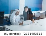 Man and woman with traditional clothes working in a business office of Dubai. Portraits of  successful entrepreneurs businessman and businesswoman in formal emirates outfits. Concept about middle east