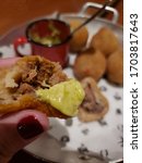 Small photo of In the foreground hand holding open coxinha appearing meat filling and mayonnaise sauce. In the background, vintage bowl with Brazilian "Coxinha de chicken" or "Carne Seca" snack and sauce. Brazilia