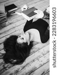 Small photo of A relaxed woman underlie and reads in a room full of books. Black and white.