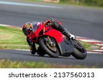 Small photo of Motorcycle rider riding on a red sport bike through the corner at high speed.