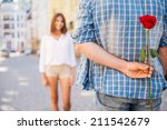 Surprise for her. Rear view of young man holding red rose behind his back while woman walking in the background 