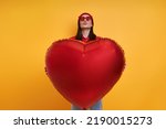 Happy young woman holding heart shape balloon against yellow background