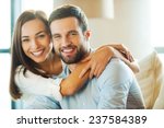 Enjoying every minute together. Beautiful young loving couple sitting together on the couch while woman embracing her boyfriend and smiling 