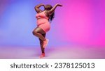 Small photo of Full length of joyful voluptuous African woman in sportswear dancing and smiling