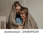 Beautiful young loving couple covering with a cozy warm blanket while spending time at home together