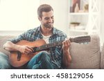 Enjoying carefree time at home. Happy young man playing the guitar while sitting on sofa at home