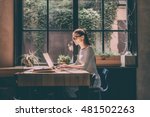 Concentrated at work. Confident young woman in smart casual wear working on laptop while sitting near window in creative office or cafe