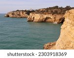Limestone cliffs, one with a small town, next to the Atlantic Ocean on a sunny winter day along the Seven Hanging Valleys Trail in southern Portugal.