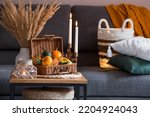 Small photo of Cozy autumn concept. Home warmth in cold weather. Still-life. Pumpkins, wicker basket, candles and flowers on the coffee table in the home interior of the living room.