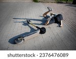 Small photo of Careless man felt down from electric scooter. Young male lying on back after falling from his vehicle. Mused male collided with a car and hurted his back.