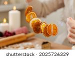 Pretty smily young woman making handmade garland from dry oranges for christmas tree decoration. Concept of holiday homemade craft and presents, zero waste, natural decor, aromathepary.