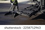 Small photo of Worker wearing protective boots and clothing smoothes fresh slurry seal
