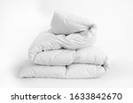 Folded soft white duvet, blanket or bedspread, against white background. Close up photo