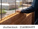 Small photo of Builder carefully puts red brick on the masonry. Quick work bricklayer. Guy measures level masonry. Man is building brick wall. Correctly calculate material. Builder manually carries brick structure