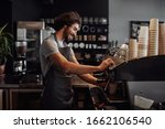 Smiling man with apron preparing coffee for customer in his small business