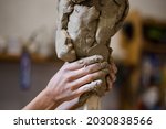Female hands create a clay head sculpture in art studio
