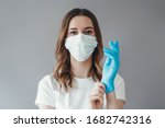 Young woman patient in a medical mask puts on protective surgical sterile gloves on her arm, isolated on gray background, protection against coronovirus