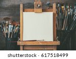Artistic equipment in a artist studio: empty artist canvas on wooden easel and paint brushes Retro toned photo.