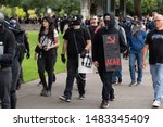 Small photo of Portland, OR / USA - August 17 2019: Group of masked Antifa demonstrators wearing black clothes at the downtown protest. One carries banner that shows hammer and sickle with ACAB written on it.