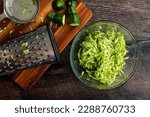 Shredded Zucchini in a Glass Mixing Bowl: Grated zucchini shown with a box grater and other tools