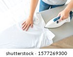 Female hands ironing white shirt collar on ironing board, view from above