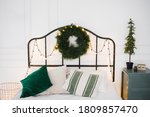 Christmas and new year composition. Scandinavian bedroom with white and green bed linen with Christmas decorations made of fir branches, garlands and a wreath.