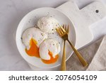 Small photo of Three poached eggs with egg yolk on a white plate on a marble board and golden forks
