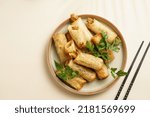 Small photo of Traditional southeast asian starter dish spring or summer rolls - deep fried dim sum dumplings stuffed with vegetables with soy sauce, fresh coriander on grey plate with black chop sticks, top view