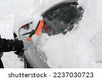 Cleaning snow from the side window of a car with a brush during a snowfall. A snow cyclone clearing snow from a car. Road safety concept.