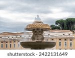 Small photo of Roma, Latium - Italy - 11-26-2022: A tranquil fountain before the Vatican's austere architecture, water cascading under Rome's overcast heavens