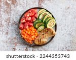Grilled chicken zucchini carrot tomato vegetables salad in plate on white wood background top view, healthy food concept.  