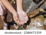 Small photo of A young girl cradles refreshing water in her hands, poised to quench her thirst.