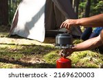 Cooking, heating a tourist kettle on a portable gas burner with a red gas cylinder. Camping, a man cooks breakfast outdoors. Summer outdoor activities