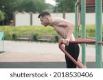 Attractive Caucasian young brunette man in sportswear doing push-ups on the bars at a playground on a warm summer day. Sports, workout, health, body care.