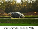 Small photo of Driving fast on a road surrounded by greenery in a modern hatchback. Side view of modern hatchback moving on the highway.