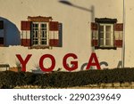 A yoga house in the village of Poertschach at the Woerthersee in Carinthia, Austria. The sun is hitting the walls of the house. The window blinders are open. Big yoga sign in front of the building