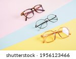 multiple eyeglasses on a multicolored background of pastel colors, geometric background, pink yellow and light blue colors, trendy eyeglass frames copy space