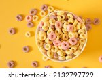 Small photo of colored breakfast cereals laid out in a bowl on a yellow background top view, children's healthy breakfast cereals laid out in the shape of a smiley face